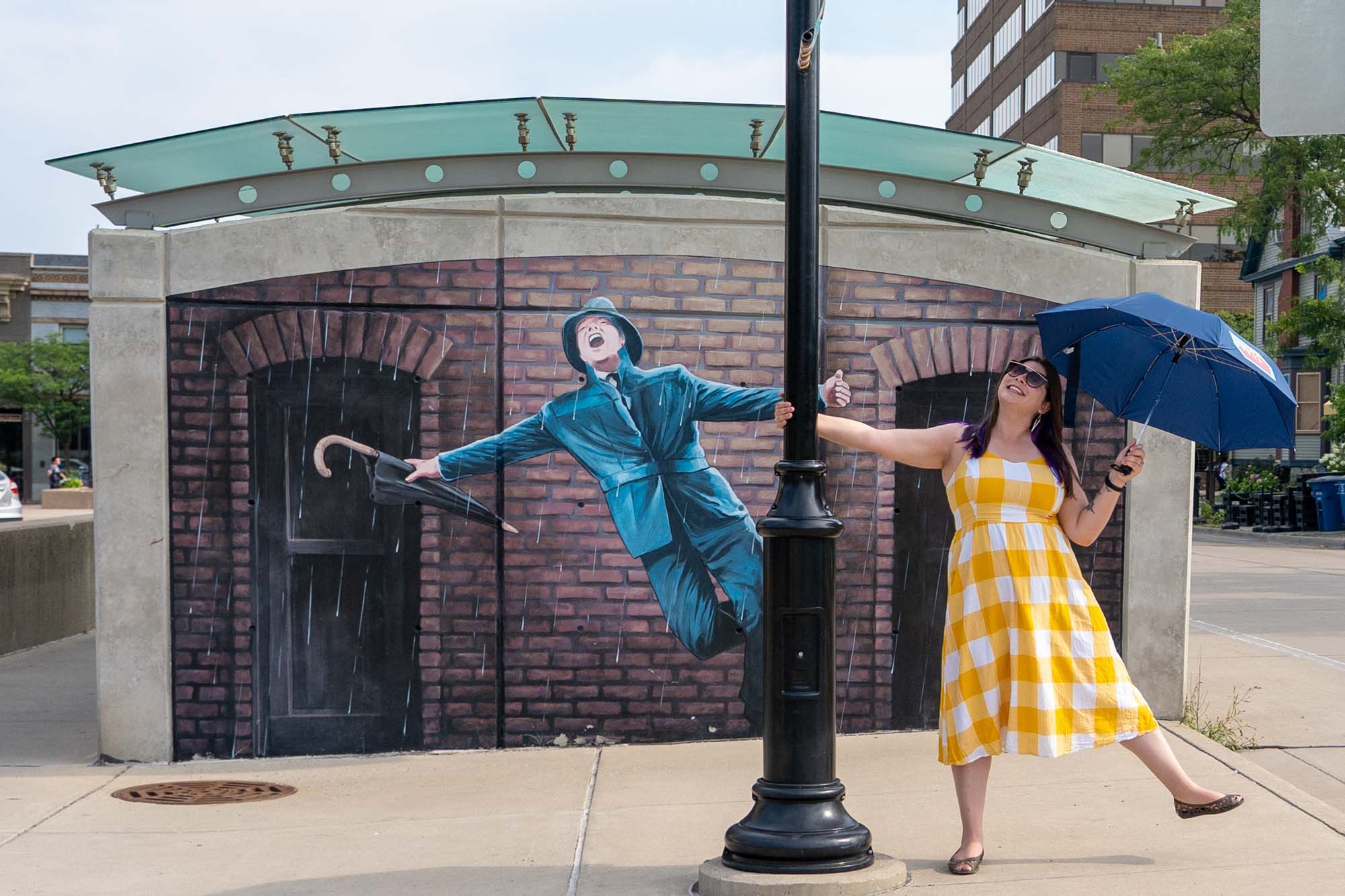 Girl with umbrella in front of the Singing in the Rain mural in Ann Arbor