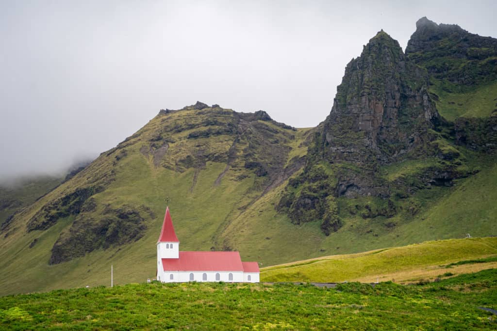 Small white church with a red roof with tall mountains behind it