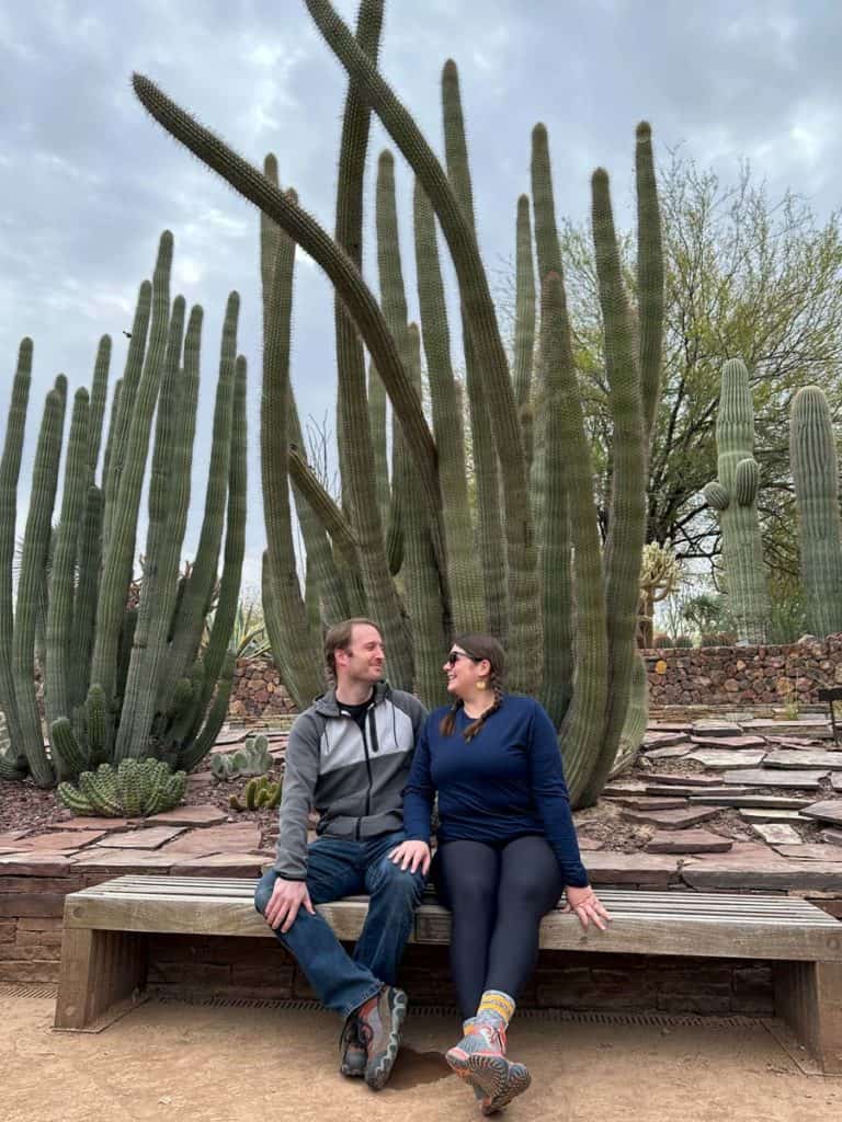 Amanda and Elliot sitting on a bench in front of a tall cacti at Desert Botanical Garden