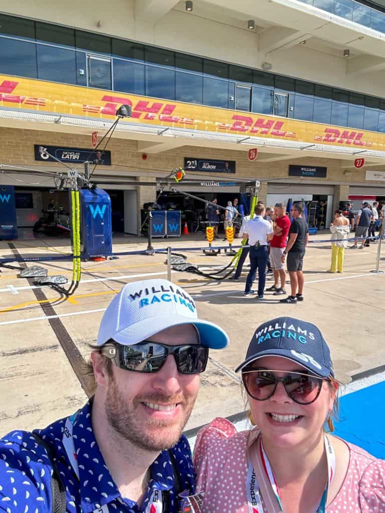 Amanda and Elliot wearing Williams hats outside the Williams pit garage