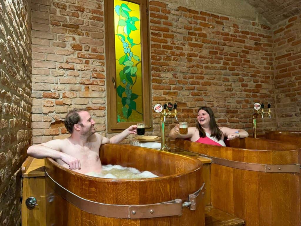 Amanda and Elliot in separate hot tubs, cheers'ing with beers